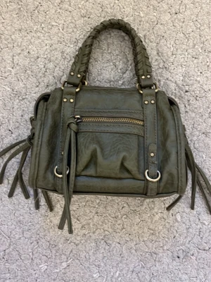 Olivgrön handväska med flätade handtag - Snygg olivgrön handväska i fejkläder med flätade handtag och dekorativa dragkedjor. Väskan har detaljer i mässingsfärgad metall och fransar på sidorna för en cool look. Perfekt storlek för det viktigaste och enkel att matcha till olika outfits. Små defekter som man inte märker vid blotta ögat. Priset går att diskuteras.