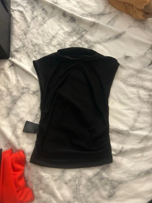 Svart ärmlös polotopp - Snygg svart ärmlös polotopp i mjukt material. Toppen har en hög krage och en slim passform som sitter snyggt på kroppen. Perfekt att styla med jeans eller kjol för en trendig look.