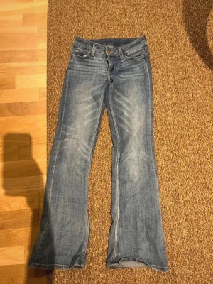 Blå bootcut jeans med slitningar - Säljer ett par klassiska blå bootcut jeans med snygga slitningar framtill.låg midja och är tillverkade i denim. Perfekta för dig som gillar en avslappnad men ändå trendig look.    De är lite smutsiga nere vid fotändan och en fläck mitt på byxan som troligen går bort i tvätten!!