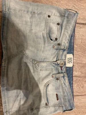 Ljusblå jeanskjol från BDG - Snygg ljusblå jeanskjol från BDG med klassisk femficksdesign och rå kant nedtill. Kjolen har en normal passform och är tillverkad i slitstarkt denimtyg. Perfekt för dig som gillar en avslappnad och trendig stil.