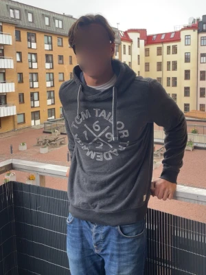 Vintage hoodie från Tom Tailor - Snygg mörkgrå hoodie från Tom Tailor med stort vitt tryck framtill. Tillverkad i mjukt material. Perfekt för en avslappnad vintage look, Modellen är 190 cm och storleken är L. 