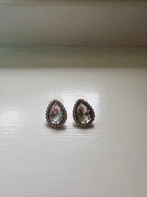 Diamant droppformade örhängen - Säljer ett par droppformade örhängen med stora, klara stenar i mitten och små gnistrande stenar runtom. Örhängena är silvriga och har en elegant, glittrig look..