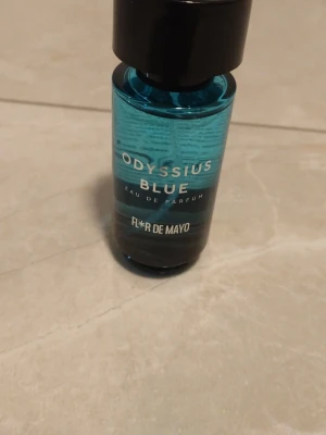 Odysseus Blue Eau de Parfum - Odysseus Blue Eau de Parfum från Flor de Mayo i en stilren blå glasflaska med svart kork. Flaskan har en modern, rund form och text i vitt och silver. Perfekt för dig som gillar fräscha och maskulina dofter.