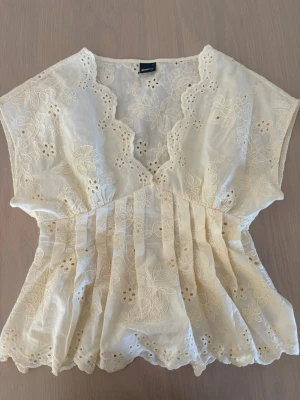 Broderad blus från Gina Tricot - Söt ljusgul blus från Gina Tricot med broderade blommor och volangkant. Blusen har v-ringning, korta ärmar och ett luftigt, flowy material som känns perfekt för varmare dagar. Romantisk och feminin look med fina spetsdetaljer.