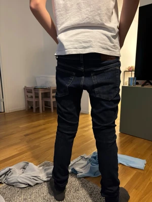 Mörkblå slim fit jeans herr - Snygga mörkblå jeans i slim fit-modell med klassiska fem fickor och kontrastsömmar. Jeansen har normal midja och smala ben som sitter tight hela vägen ner. Perfekta för dig som gillar en stilren och enkel look.