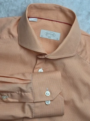 Eton Slim skjorta smårutig orange/vit storlek S 38/15 - Eton Slim skjorta smårutig orange/vit storlek S 38/15  Smårutig skjorta från Eton i Slim-passform. Stilren orange och vit design med diskret microcheck-mönster och vita knappar. Klassisk modell som fungerar både till vardag och mer uppklätt. Tillverkad i 100% bomull.  Storlek S / 38 / 15 Slim Fit  Mycket fint skick.  Mått Bröstbredd: ca 50 cm Plagglängd: ca 76 cm Axelbredd: ca 44 cm Ärmlängd: ca 65 cm  Material 100% bomull  Varan är begagnad och säljs i befintligt skick, se bilder för detaljer.