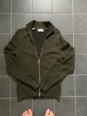 Olivgrön ziptröja Selected Homme - Snygg olivgrön ziptröja från Selected Homme i storlek M. Tröjan har hög krage, grovstickad struktur och dragkedja hela vägen. Perfekt till lager på lager och enkel att matcha med jeans eller chinos.