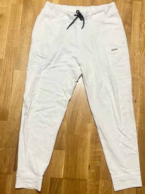 Vita mjukisbyxor från Hugo - Snygga vita mjukisbyxor från HUGO med svart dragsko i midjan och diskret logga på benet. Byxorna har avsmalnande ben och muddar vid bensluten. Perfekta för en chill och stilren look. Tillverkade i mjukt material för maximal komfort.