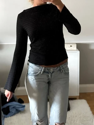 Svart långärmad topp med struktur - Säljer en svart långärmad topp med snyggt strukturerat tyg och rund halsringning. Toppen har en normal passform och är perfekt att styla med jeans eller kjol. Materialet känns mjukt och följsamt mot kroppen. PRISLAPP KVAR!