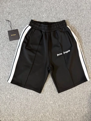 Svarta shorts från Palm Angels - Svarta shorts från Palm Angels med vita sidoränder och logga på vänster ben. Aldrig andvända. Hör av dig vid frågor eller behov av fler bilder!🤗☺️