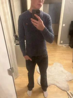 Blå kabelstickad tröja - Snygg blå kabelstickad tröja med rund hals och ribbade muddar. Tröjan har ett diskret broderat märke på bröstet och är perfekt för dig som gillar klassisk stil med en modern twist. Passar lika bra till jeans som till chinos. Tröjan är i storlek XS men passar S och M. Själv är jag 184cm lång. 