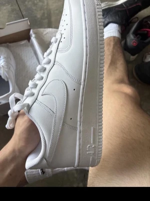 Vita Air force 1 - Säljer ett par helvita sneakers med låg profil och stilren design. Skorna har en tjock sula, perforerade detaljer på tån och är tillverkade i slätt läder. Perfekta för dig som gillar en clean och tidlös look. Dom är i ny skick fått de i present, har redan ett par så därför ska dom säljas