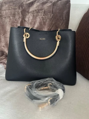 Elegant svart väska från Aldo  - Jättefin och elegant handväska ifrån Aldo. Den är i bra skick utöver att lite färg släppt från handtagen (se bild 3) men inget jag tänkt på!Axelrem medföljer också. Nypris från Zalando 729:-. 🫶🏼