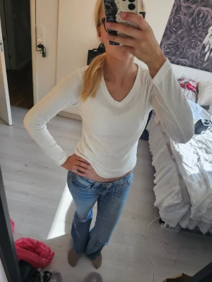 Vit ribbad långärmad tröja - Snygg vit långärmad tröja med ribbad struktur och v-ringning. Tröjan har en kroppsnära passform och är perfekt att matcha med jeans. Enkel och stilren design som passar till många olika looks.