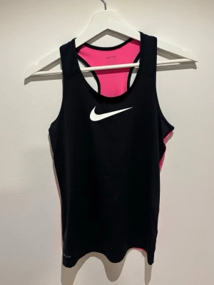 Svart och rosa träningstopp från Nike - Snygg sporttopp från Nike i svart med rosa rygg och vita loggan framtill. Aldrig använd, stl L barn vilket blir ca S