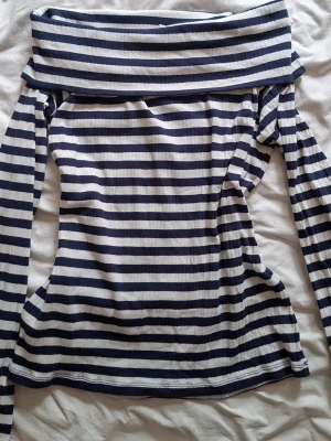 Randig offshoulder topp från Lindex - Säljer en ribbad offshoulder topp från Lindex i marinblått och vitt. Toppen har långa ärmar och ett brett axelparti som ger en snygg offshoulder-look. Perfekt för dig som gillar klassiska ränder och vill ha en bekväm men trendig topp.