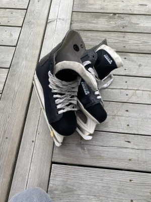 Svarta hockeyskridskor från Canada - Säljer ett par klassiska svarta hockeyskridskor från Canada med vita snören och vit insida. Skridskorna har robust konstruktion och tålig plast runt sulan. Perfekta för isbanan eller spontanhockey med vänner.