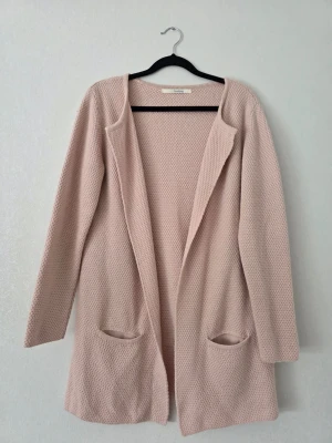 Ljusrosa lång kofta med fickor - 🌸 Fin lång stickad kofta från Sibin Linnebjerg i en mjuk puderrosa nyans. Öppen modell med strukturerad stickning och två fickor framtill. Innehåller 50 % merinoull.  🔖 Stl S 📏 Byst ca 53 cm Axel ca 41 cm Innerärm ca 47 cm Längd ca 78 cm  🧵 50 % merinoull, 50 % akryl  ✨ Sparsamt använd och i mycket fint skick utan anmärkningar.  🏷️ Nypris ca 1 499 kr  🩶 Finns även i mörkgrått i separat annons.