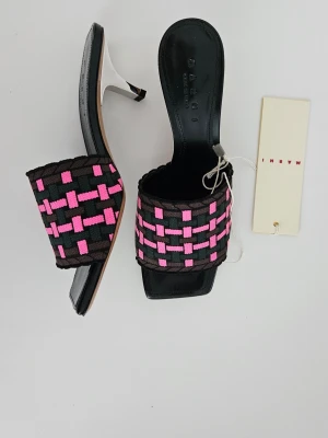 Unika Marni mules med klack - Unika mules med klack från Marni med svart bas och bred rem i vävt tyg med rosa och brunt rutmönster. Skorna har öppen tå, fyrkantig framdel och smal klack. Perfekta för dig som vill sticka ut med en cool och trendig look.