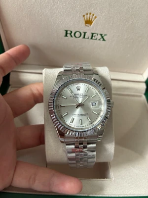 Datejust med silverfärgad urtavla  - Ny Datejust med silverfärgad urtavla och komplett uppsättning. Högkvalitativt automatiskt urverk med nattbelysningsfunktion. Urtavlan är 41 mm i diameter, med Jubilee-armband och Oyster-spänne. Levereras med ask och tillbehör. Perfekt för den som älskar lyxiga accessoarer.