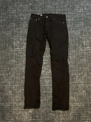 Levis 511 - Säljer ett par svarta slim fit jeans med klassisk femficksdesign och raka ben. Jeansen har silverfärgade nitar och knapp, samt en liten röd detalj på bakfickan. Perfekta för en clean och stilren look. Jeansen är i storlek W29 och L34