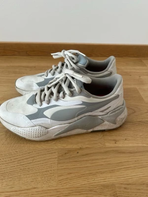 Vita och grå Puma Golfskor 42,5 - Säljer ett par vita och grå sneakers med chunky sula och sportig design. Skorna har snörning och detaljer i olika nyanser av grått. Perfekta för dig som gillar en modern och avslappnad stil. Materialet är syntet och textil.