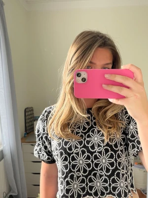 Svart croppad topp med blommönster - Säljer en svart croppad topp med vita blommor i ett broderat mönster. Toppen har korta puffärmar och vågig kant nertill. Perfekt för dig som vill ha en trendig och unik look.