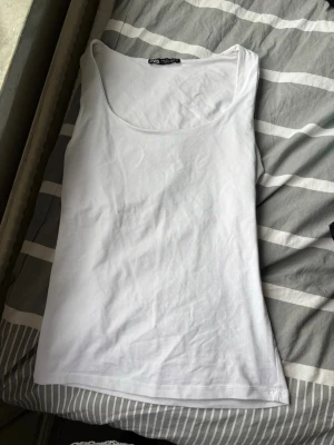 Vit baslinne från Zara - Säljer ett vitt baslinne från Zara med rundad halsringning och smala axelband. Perfekt att styla till jeans eller kjol. Tillverkat i mjukt och stretchigt material som känns skönt mot huden.