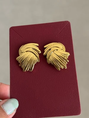 Guldtonade vintage örhängen - Säljer ett par snygga örhängen i guldtonad metall med flätad, strukturerad design. De har en cool retrostil och är perfekta för dig som gillar statement-smycken. Passar till många olika looks och ger en lyxig känsla.