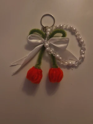 Nyckelring med pärlor och blommor - Söt handgjord nyckelring med pärlarmband och två blommor i piprensare, en med röda och en med vita blommor. Dekorerad med vit rosett och pärlor. Perfekt som accessoar till väskan eller nycklarna. Finns i flera andra färger! 