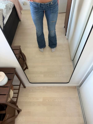 Blå bootcut jeans med slitningar - Säljer ett par ljusblå bootcut jeans med slitningar på låret och knät. Jeansen har klassisk femficksmodell, normal midja och är i ett mjukt denimtyg. Jag är 176 cm och de passar parfekt i längden för mig🥰🥰
