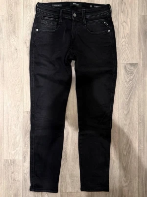 Replay Anbass Hyperflex Svarta Jeans W29/L30 - Slim Fit - Replay Anbass Hyperflex svarta jeans med slim fit-passform som sitter smalt och bekvämt och funkar till allt, storlek W29/L34 men passar L30, midja 38 cm, ytterbenslängd 98 cm, benöppning 15 cm, modellen är 185cm & väger 65kg, i fint skick.