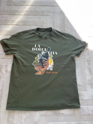 Grön Ardbeg t-shirt: Limited edition - Säljer en Limited Edition grön t-shirt med tryck fram och bak. På framsidan står det 'La Dolce Vita' och bild med Ardbeg whisky. På baksidan står det 'Ardbeg Day 2026'. Riktigt snygg och unik. Helt ny med alla lappar kvar. 