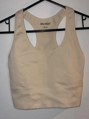 Beige ribbad sport-topp Gina Tricot - Säljer en beige ribbad sport-BH från Gina Tricot i storlek XXS/XS. Bh:n har breda axelband och brottarrygg för extra stöd och komfort. Perfekt för träning och har en stilren, enkel design.
