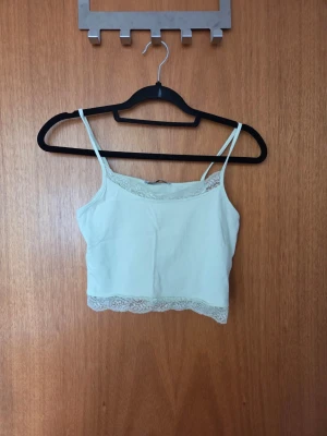 Ljusgrön croppad linnetopp med spets - Söt ljusgrön croppad linnetopp med tunna axelband och spetsdetaljer längs halsringning och nederkant. Perfekt för varma dagar eller som layering-piece. Enkel och stilren design som passar till mycket.