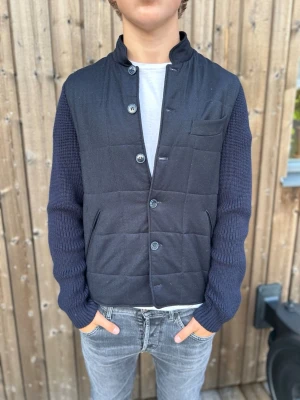 Studio 73 marinblå cardigan  - Snygg marinblå dunväst med quiltat mönster och stickade ärmar från Studio 73. Västen har knäppning framtill med fem knappar, två sidofickor och en bröstficka. Perfekt för lager-på-lager och ger en modern look till din outfit. Det är en sjukt snygg cardigan som passar på fin evenemang eller bara casual. Cardiganen har kostat 4500kr som ni ser på sista bilden och den är limited edition alltså går inte att köpa längre. Modellen är 179 storleken är 48/48 men passar M/S