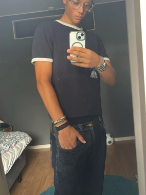 Mörkblå t-shirt med vita detaljer - Säljer en stilren mörkblå t-shirt med vita kanter vid ärmslut och halsringning. T-shirten har en klassisk passform och är perfekt för en enkel och clean look. Materialet känns mjukt och skönt mot huden.