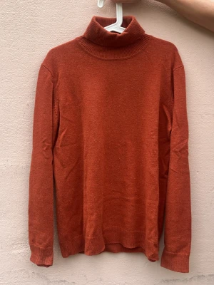 Rostfärgad polotröja stickad - Snygg rostfärgad stickad polotröja med lång ärm och ribbade muddar. Tröjan har en hög polokrage och är i mjukt material, perfekt för kyligare dagar. Enkel och stilren design som passar till det mesta.
