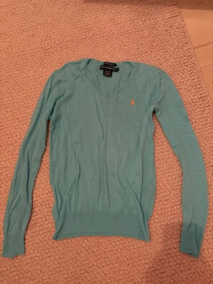 Ljusblå stickad tröja Ralph Lauren - Ljusblå stickad tröja från Ralph Lauren Sport med boyfriend fit. Tröjan har V-ringning, långa ärmar och en liten broderad logga på bröstet. Tillverkad i bomull och lin. Supercool och unik. Perfekt för en avslappnad och stilren look. Det står inte vilken storlek det är men skulle säga ungefär M