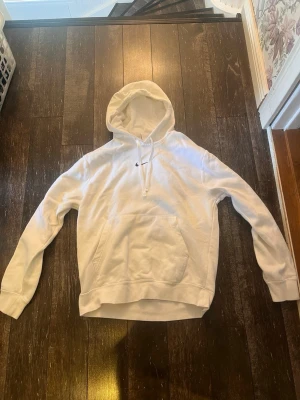 Vit Nike hoodie med ränder - Säljer en vit hoodie från Nike med huva och känguruficka. På ärmarna finns röda och blå ränder med Nike-loggor längs sidorna. Klassisk Nike Swoosh broderad på bröstet. Hoodien har ribbade muddar och dragsko i huvan. Perfekt för en sportig och avslappnad stil. Skriv om ni har frågor!