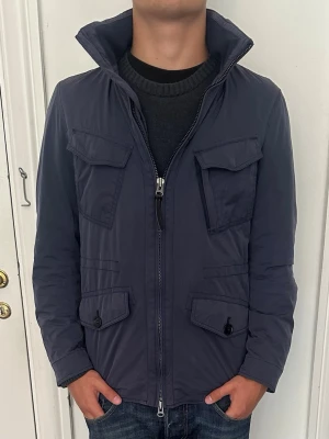 Woolrich - Fieldjacka - Snygg jacka från woolrich i storlek Small. Dubbla dragkedjor samt en luva som går att veckla ut. Bra skick utöver en liten skada på högerarm, sista bilden
