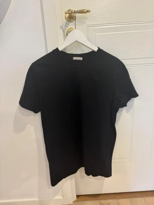 Moncler tshirt - Säljer min svarta Moncler T-shirt i storlek M. Stilren design med Moncler-loggan placerad på sidan av armen. T-shirten är i mycket bra skick och passar perfekt till en clean och stilren outfit.