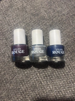 Nagellack trio från Atelier Rouge - Säljer tre snygga nagellack från Atelier Rouge i olika färger: mörklila, glittrigt silver och djupblå. Flaskorna har rund form och vita lock. Perfekt för dig som vill variera din nagelstil med trendiga nyanser.