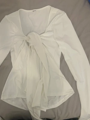Söt vit knyt topp liknar den från Gina tricot - Snygg vit blus med lång ärm och stor knytning framtill som ger en trendig look. Blusen har en djupare rundad ringning och är tillverkad i ett mjukt, lätt tyg som faller fint. Perfekt för dig som vill ha något stilrent men ändå unikt.( passar som m/s)