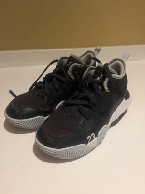 Svarta sneakers med vita detaljer - Snygga svarta sneakers med vita och grå detaljer samt siffran 23 på sidan. Skorna har en sportig design med mesh och syntetmaterial, samt en tjock, mönstrad sula för extra grepp. Perfekta för dig som gillar streetwear och basketinspirerad stil.