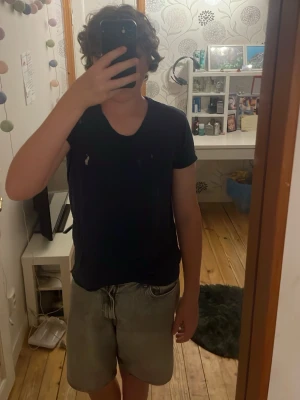 Mörkblå Ralph Lauren t-shirt med v-ringning - Snygg mörkblå t-shirt med v-ringad hals och liten broderad Ralph Lauren logga på bröstet. Klassisk passform och korta ärmar, perfekt till jeans eller shorts. Tillverkad i mjukt bomullsmaterial som känns skönt mot huden.