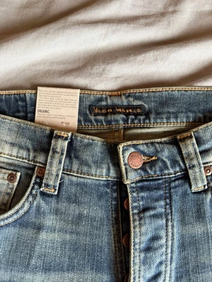 Ljusblå jeans från Nudie Jeans - Säljer ett par exklusiva och helt oanvända Nudie Jeans i modellen "Grim Tim", tvätt "Natural Worn". Prislappar och tags sitter fortfarande kvar! Nypris ligger runt 1500 kr.  Fick dessa som julklapp för ett tag sedan men de glömdes tyvärr bort i garderoben. Nu när jag väl hittade dem är de för små för mig, och eftersom returtiden har gått ut säljer jag dem vidare här till ett riktigt bra pris.   Detaljer: * Modell: Grim Tim (Slim straight fit) * Färg/Tvätt: Natural Worn (Snygg inarbetad mörkblå s