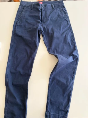Mörkblå chinos med raka ben - Snygga mörkblå chinos med raka ben och klassisk passform. Byxorna har framfickor, bälteshällor och två bakfickor, varav en med knapp. Tillverkade i mjukt bomullstyg som ger en skön känsla och stilren look.