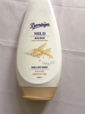 Barnängen Mild Balsam Vetprotein - Barnängen Mild Balsam med vetprotein är ett veganskt balsam som är snällt mot håret och passar känsligt hår. Flaskan är vit med beige lock och har illustration av vetekorn på framsidan. Perfekt för vård till skadat och känsligt hår för hälsosam lyster.