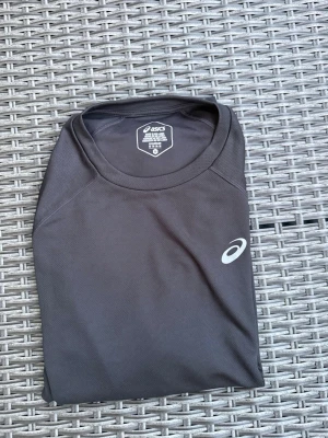 Svart tränings-tshirt från Asics - Säljer en svart tränings-tshirt från Asics i funktionsmaterial. T-shirten har rund halsringning och Asics-logga på bröstet. Perfekt för löpning, gym eller annan träning. Materialet är lätt och andas bra. I perfekt skick!